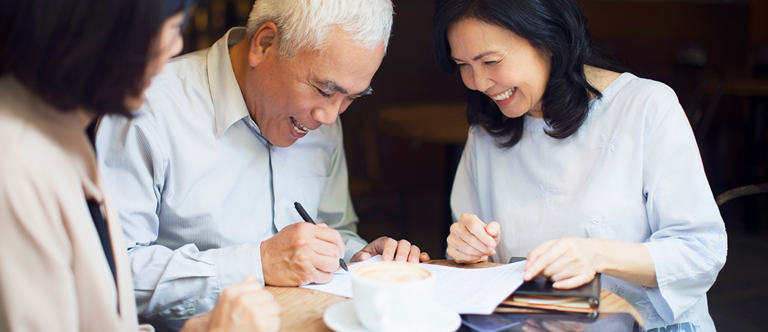 A man signs a contract while a woman smiles next to him.